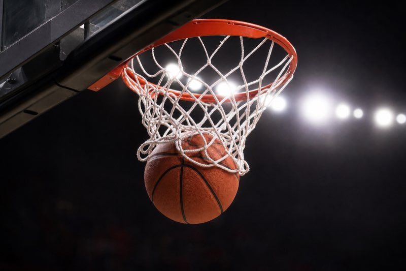 A basketball dropping through the rim and net in a darkened arena